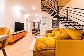 Una sala de estar con sofá, televisor, mueble de entretenimiento de madera y una escalera.