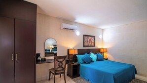 A bedroom with a bed, bedside table, lamp, and a desk with a chair.