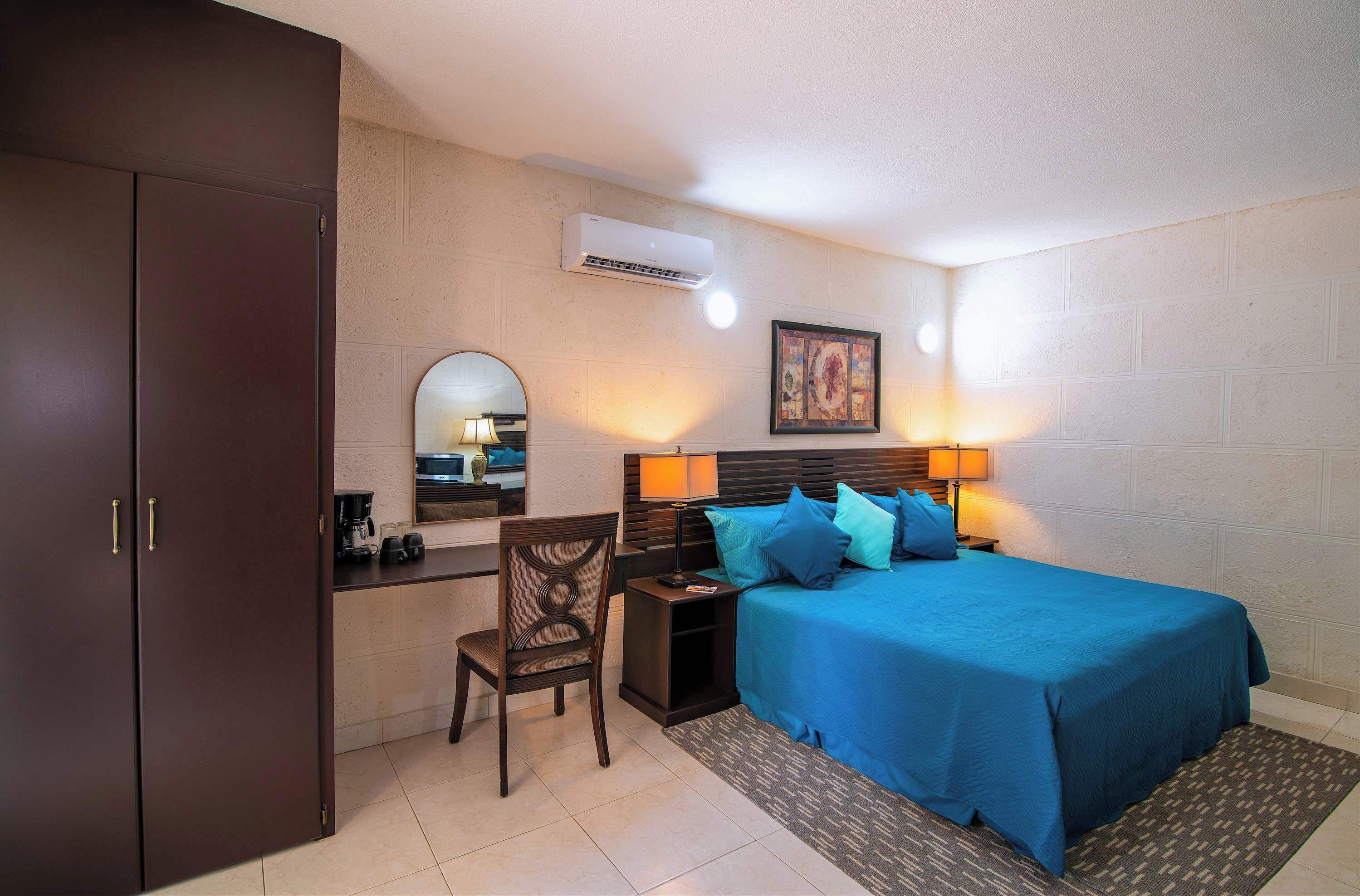 A bedroom with a bed, bedside table, lamp, and a desk with a chair.
