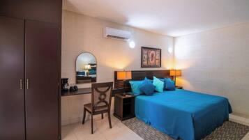 A bedroom with a bed, bedside table, lamp, and a desk with a chair.