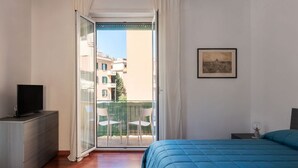A bedroom with a bed, a TV on a dresser, a balcony with chairs, and a painting on the wall.