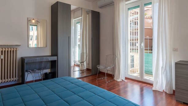 A bedroom with a bed, a chair, a radiator, a mirror, and a window with curtains.