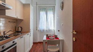 A compact kitchen with a stove, sink, and cabinets, a dining table with chairs, and a window with curtains.