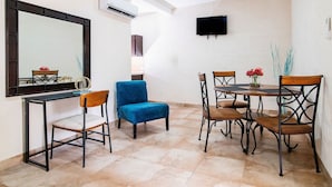A dining area with a table and chairs, a blue chair, a mirror, and a TV on the wall.