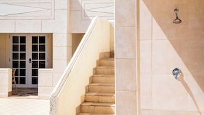 A building with a staircase leading to a door with glass panels, a tiled wall with a showerhead, and a chair outside.