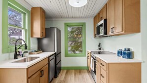 Una cocina compacta con armarios de madera, un refrigerador de acero inoxidable, un microondas y un lavamanos.