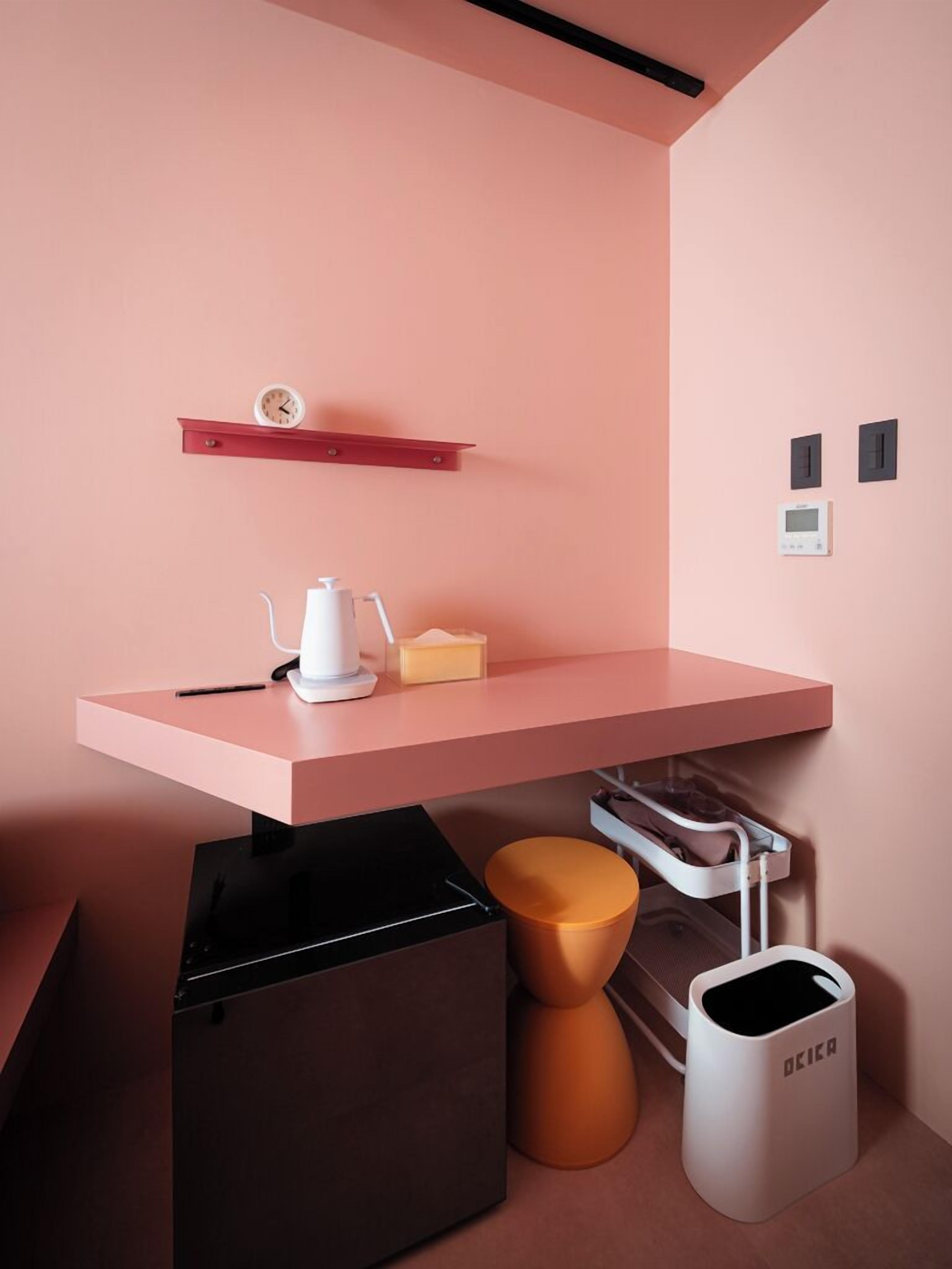 A modern kitchen with a pink countertop, a coffee machine, a small shelf with a clock, and a trash bin.