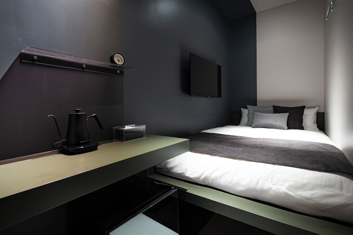 A modern bedroom with a bed, a desk, and a wall-mounted clock.