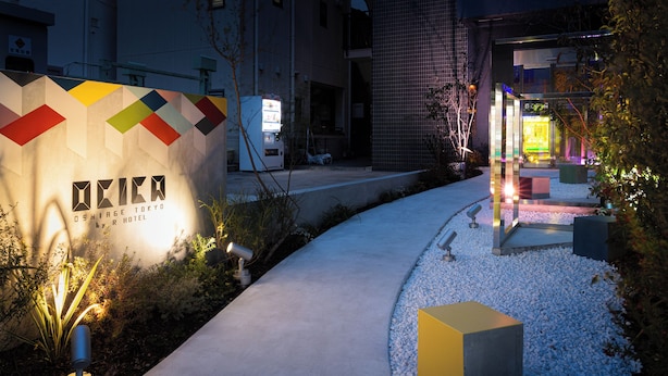 A hotel entrance with a colorful geometric sign, a pathway, and security cameras.