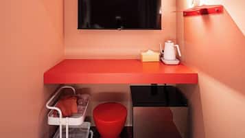 A compact kitchenette with a red countertop, a black refrigerator, a white trash bin, and a red stool.