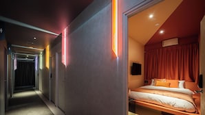 A modern hotel room with a bed, a TV, and a microwave. There is a hallway with doors and a sign indicating the room number.