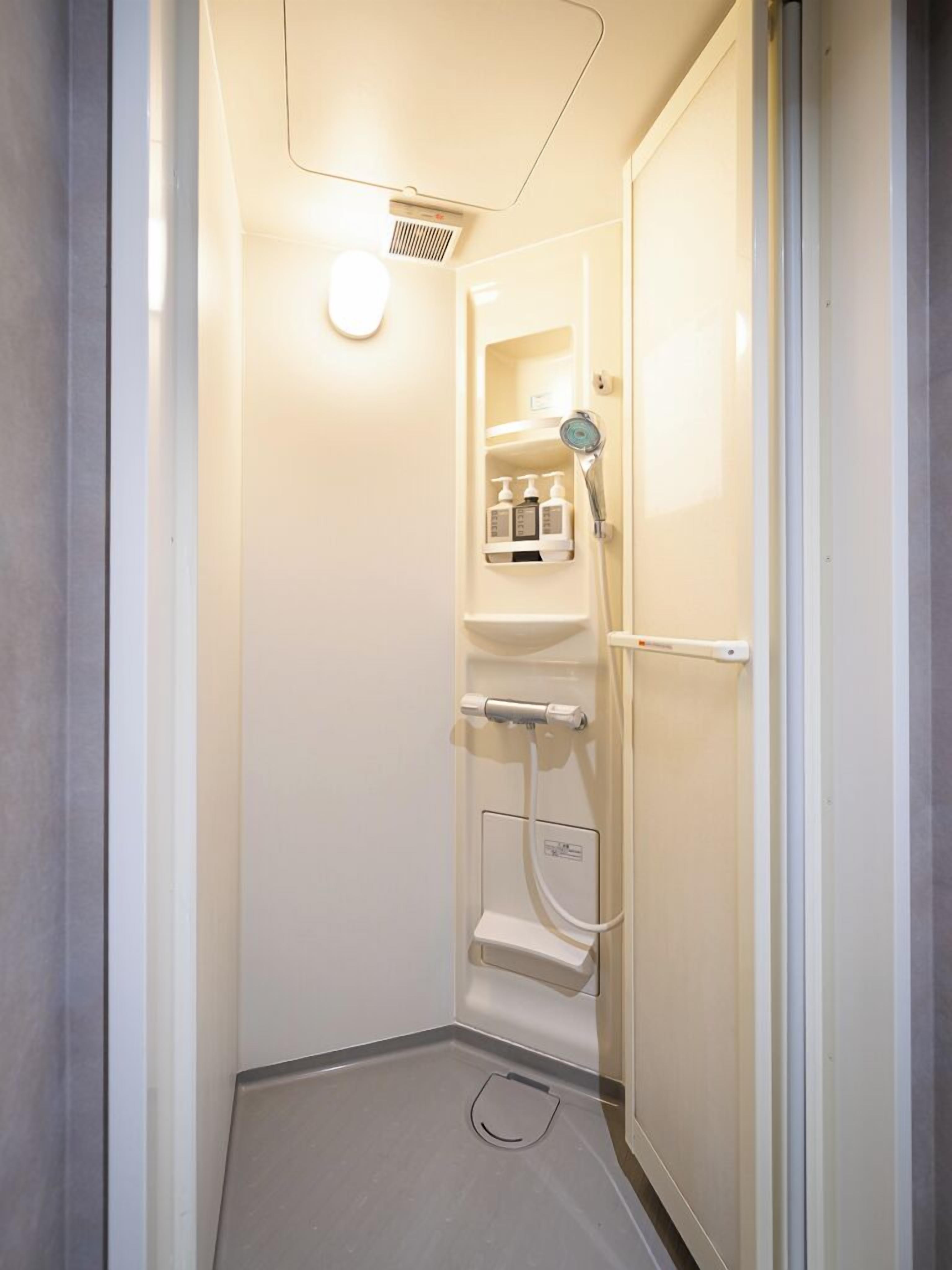 A small, enclosed shower stall with a built-in shelf holding toiletries.
