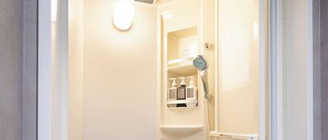 A small, enclosed shower stall with a built-in shelf holding toiletries.
