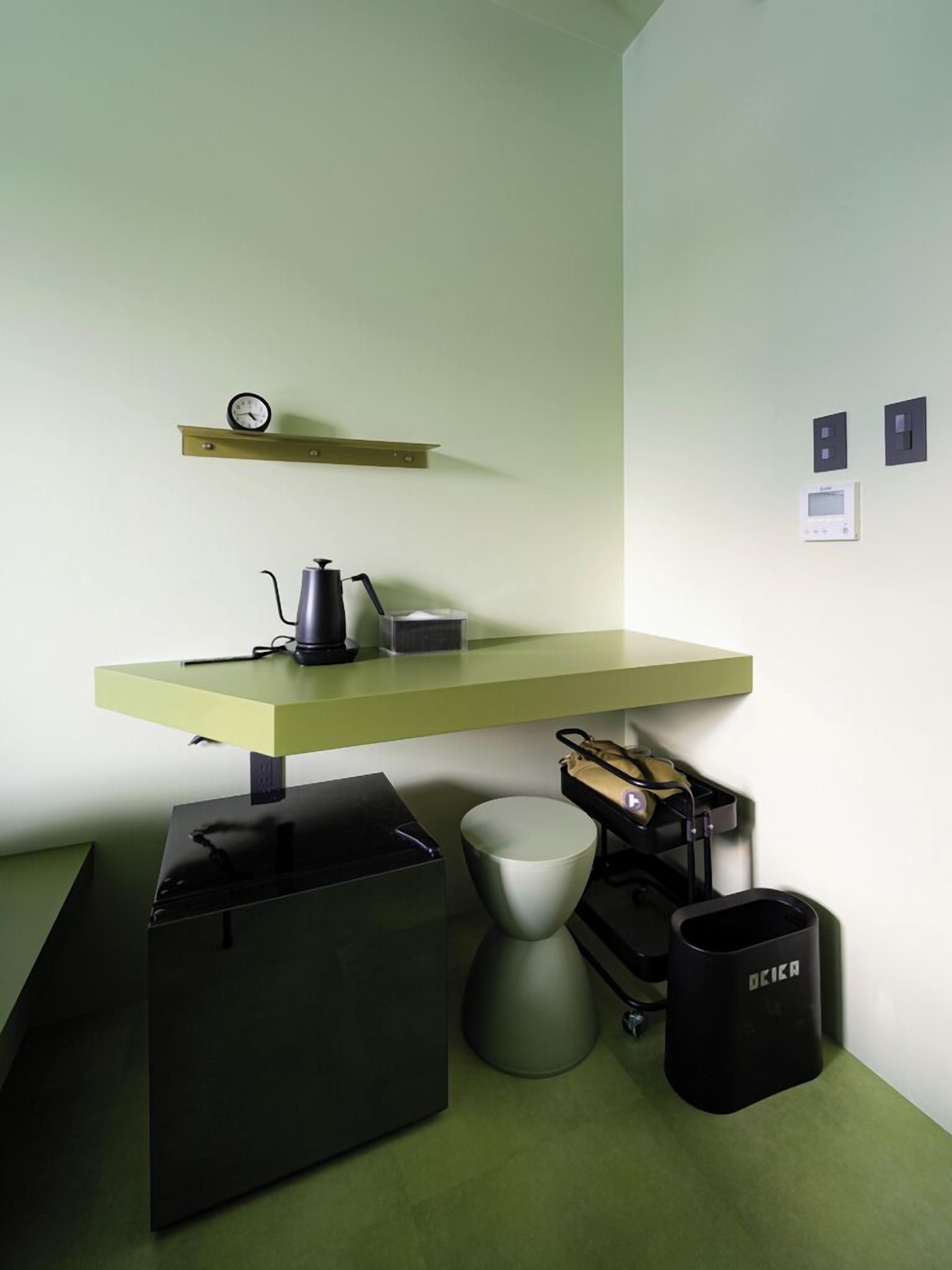 Een compacte kitchenette met een groen aanrecht, een waterkoker, een koffiezetapparaat, een prullenbak en een klein spoelgedeelte.