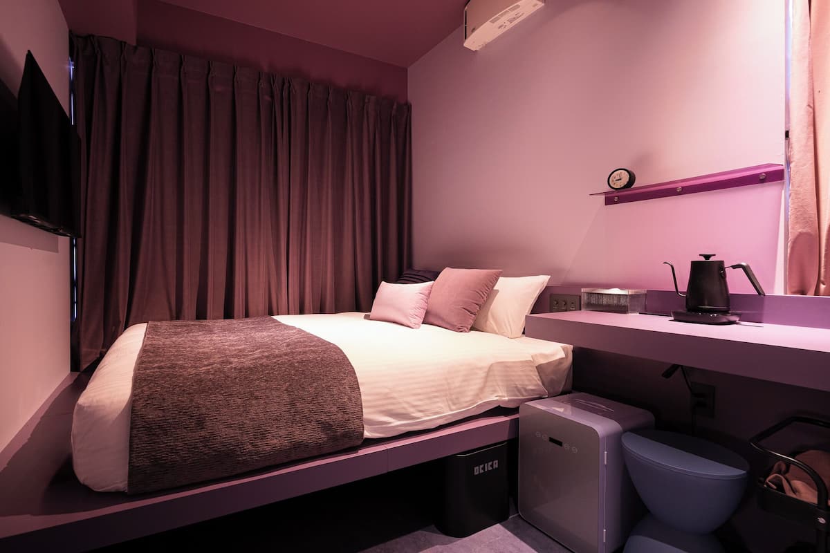 A modern bedroom with a bed, a small desk, a coffee maker, and a TV mounted on the wall.