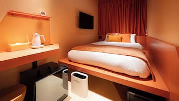 Ett hotellrum med en säng, ett skrivbord, en stol, en tv och en papperskorg.