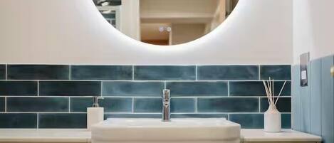 A bathroom with a white sink, a round mirror, and a blue-tiled backsplash.