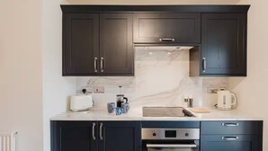 Eine moderne Küche mit dunklen Schränken, einer Marmorarbeitsplatte, einem eingebauten Backofen und einer Kaffeemaschine.