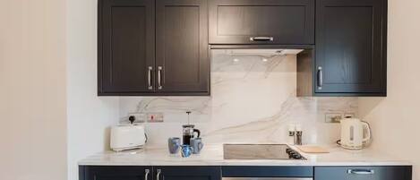 A modern kitchen with dark cabinets, a marble countertop, a built-in oven, and a coffee maker.