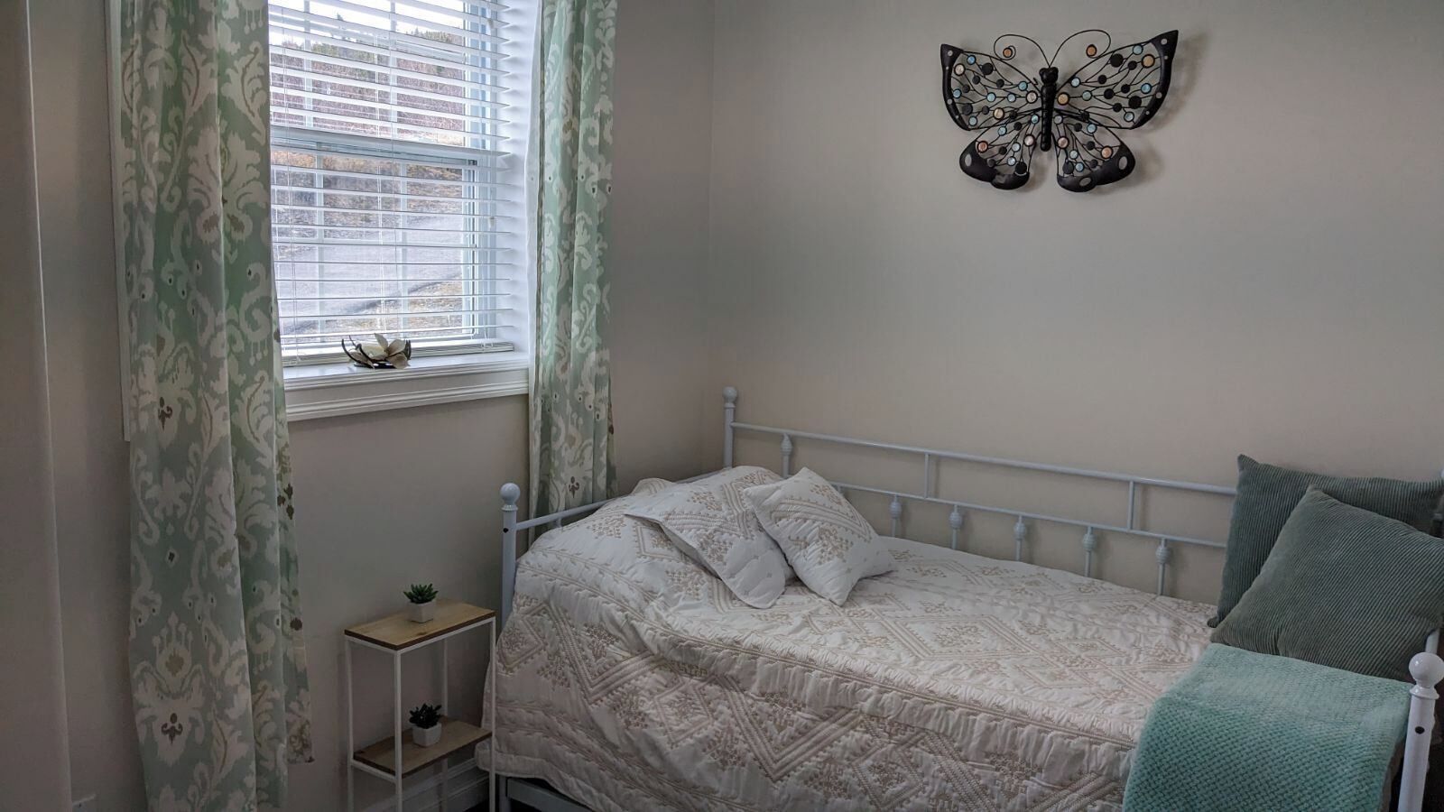 A bedroom with a bed, a nightstand, a window with curtains, and a butterfly wall decoration.