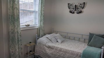 A bedroom with a bed, a nightstand, a window with curtains, and a butterfly wall decoration.