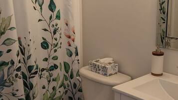 A bathroom with a toilet, a shower curtain with floral patterns, a toilet paper holder, and a cabinet with drawers.