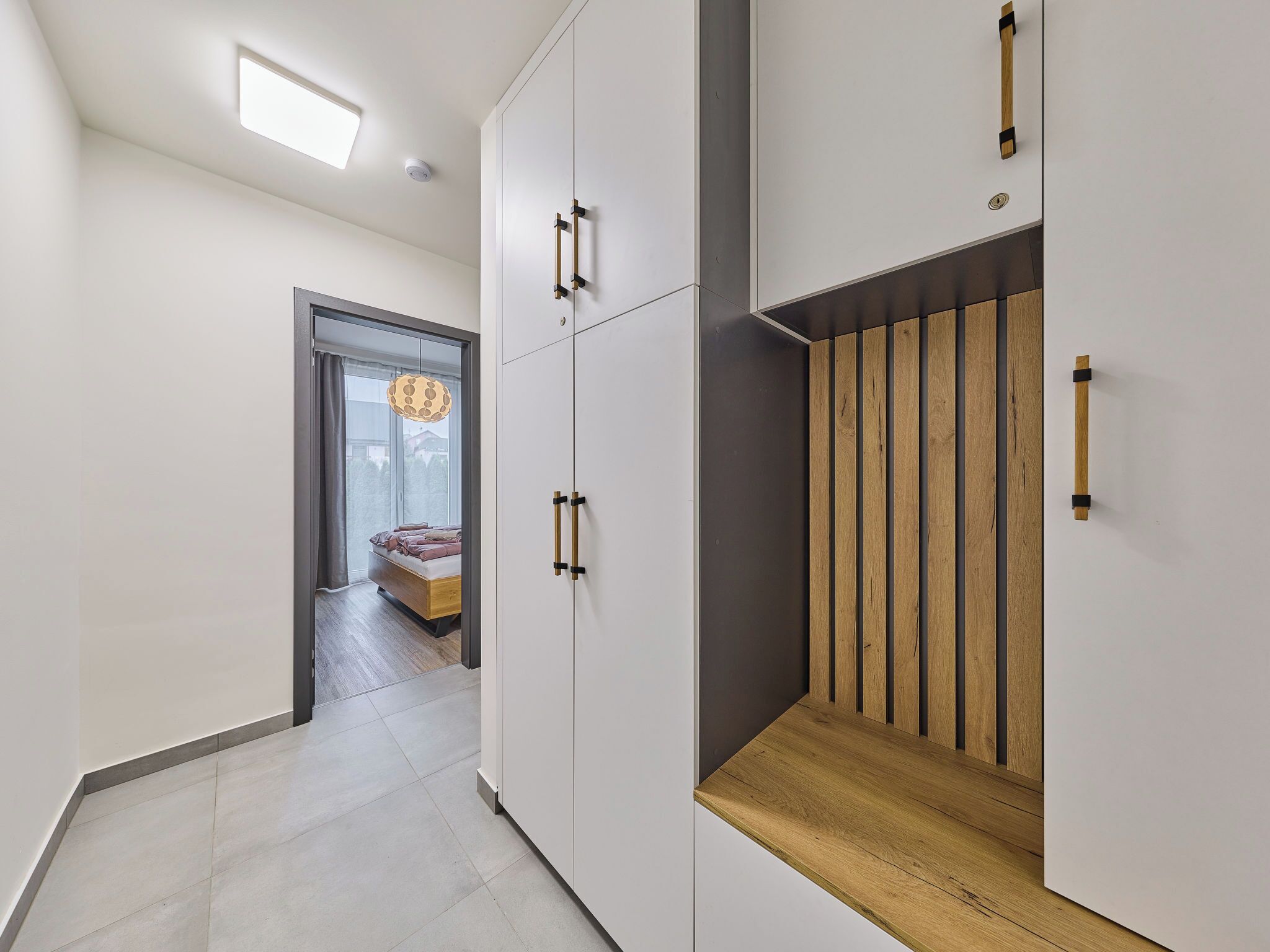 A modern interior with a hallway leading to a bedroom with a bed and a window.