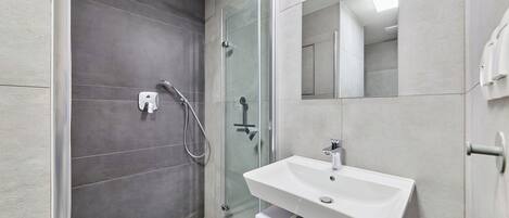 Un baño moderno con cabina de ducha de vidrio, un lavamanos blanco y un espejo grande.