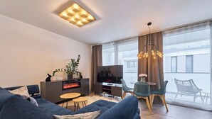 Una sala moderna con un sofá azul oscuro, un televisor de pantalla plana, una chimenea y un comedor con sillas y una mesa.