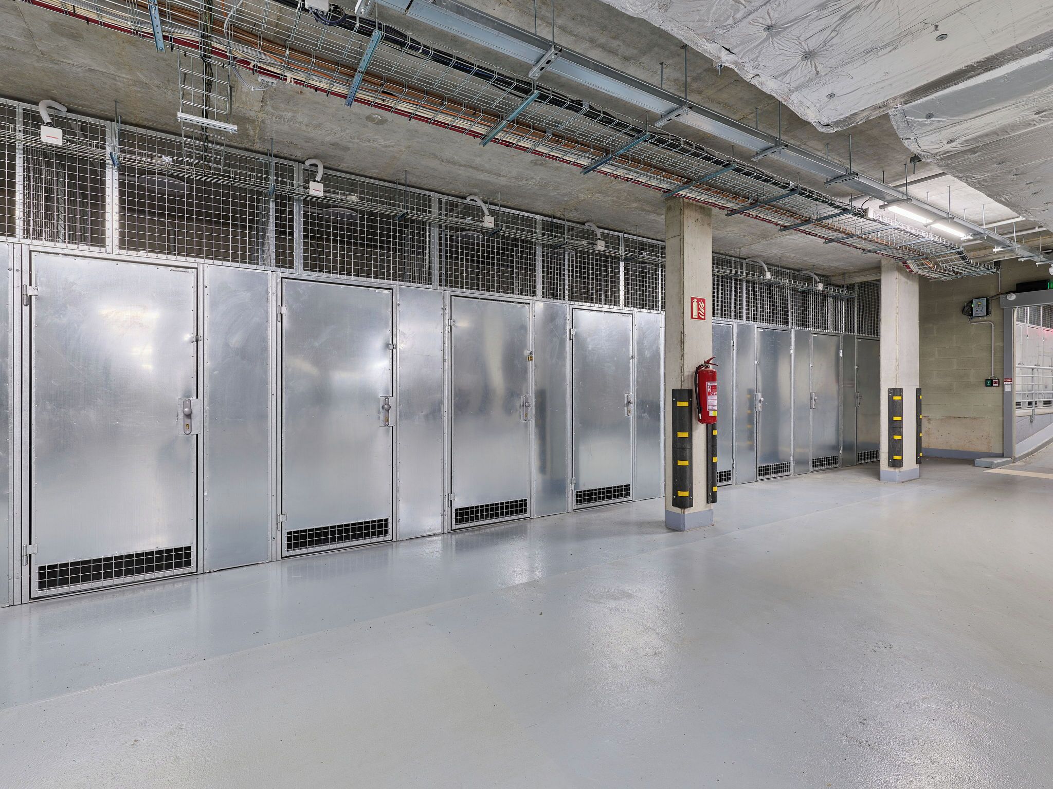 A row of metallic lockers in a clean, industrial-style room with concrete pillars and exposed pipes.