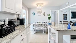 A modern kitchen with white cabinets, a marble countertop, a dining area with a patterned bench, and decorative wall art.