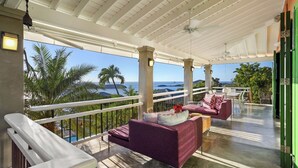 A covered outdoor area with a view of the ocean, featuring a seating area with a sofa and chairs, and a railing.