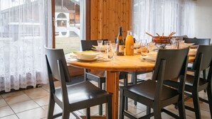 A dining area with a wooden table set for four, surrounded by chairs. There are wine glasses, a bottle of wine, and a bottle of orange juice on the table. - Austral 105 by Interhome (Ovronnaz)