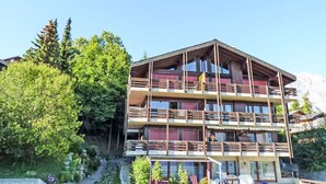A multi-story building with balconies, large windows, and a mountainous backdrop. - Austral 105 by Interhome (Ovronnaz)