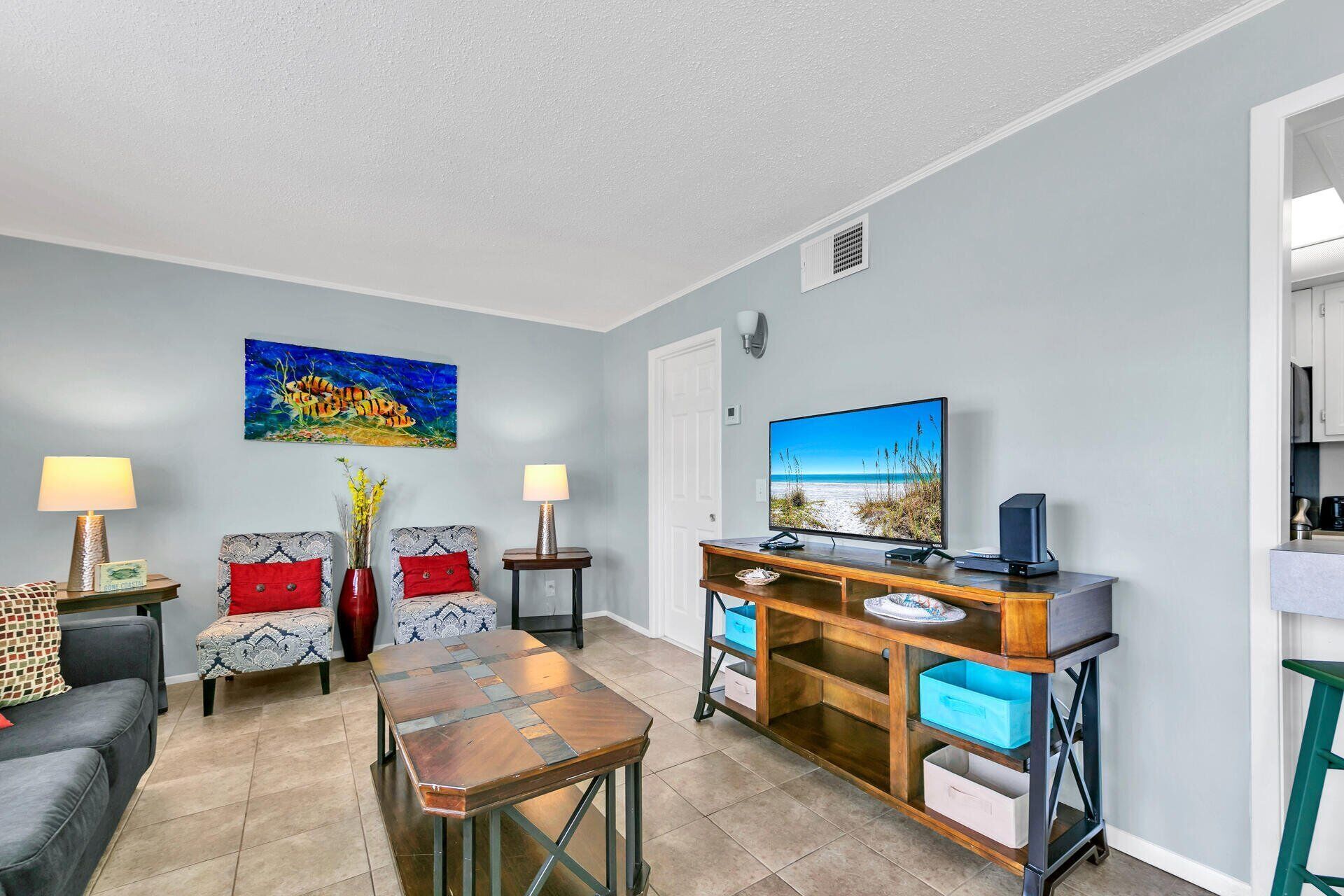 A living room with a TV, a coffee table, two armchairs, a sofa, and a side table with a lamp.