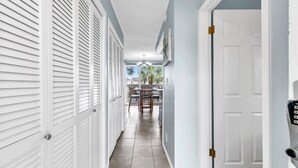 A hallway with white shutters, a dining area with a table and chairs, and a door with a keypad lock. - Sandpiper Cover 2031 near beach sleeps 4 (Destin)