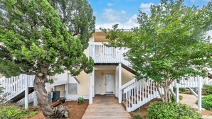A two-story building with a wooden deck leading to the entrance, surrounded by trees and a white fence. - Sandpiper Cover 2031 near beach sleeps 4 (Destin)
