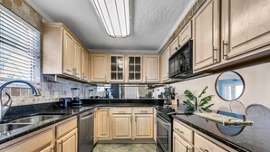 A modern kitchen with wooden cabinets, a black countertop, a stainless steel sink, and a microwave. - Destin Harbor Views & Access to Boat Dock! CP6 (Destin)