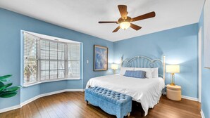 A bedroom with a bed, a ceiling fan, a window with blinds, a bedside table with a lamp, and a bench. - Destin Harbor Views & Access to Boat Dock! CP6 (Destin)