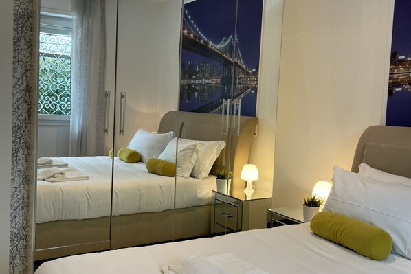 A hotel room with a bed, a nightstand, a lamp, and a large mirror reflecting the room.