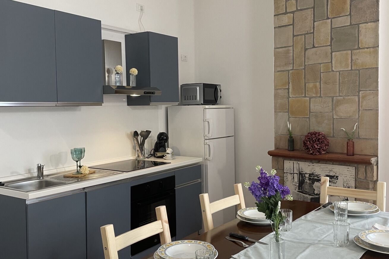 A compact kitchen with grey cabinets, a microwave, and a refrigerator. There is a dining table set with plates and glasses.