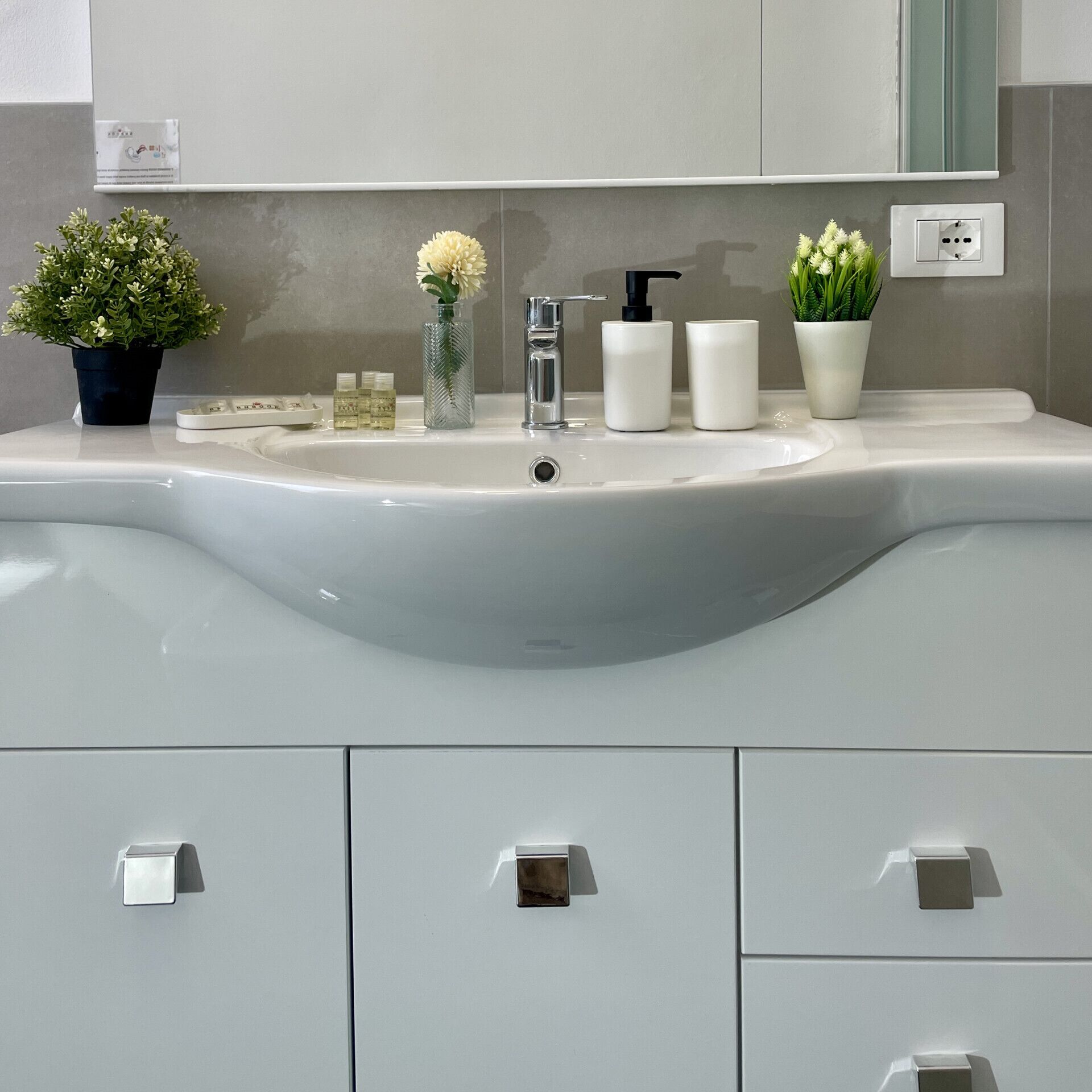 Ein Badezimmer mit einem weißen Waschbecken, einem Spiegel und drei Schubladen.