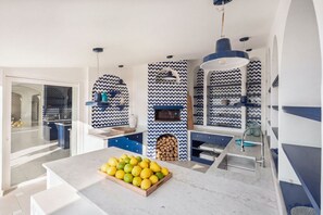 A modern kitchen with a marble countertop, a fruit bowl, and patterned backsplash.