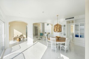 A spacious living area with a dining table, white chairs, and a hanging light fixture.