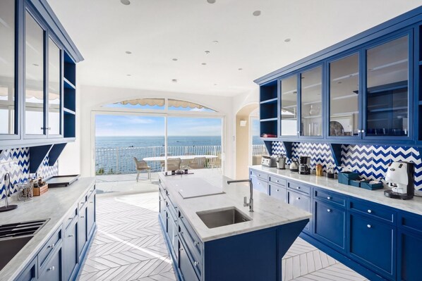 A modern kitchen with blue cabinets, a large island, and a view of the ocean.