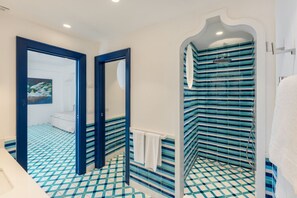 A bathroom with a checkered floor pattern, a shower with blue-striped tiles, and a white bathtub.