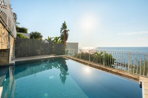 A clear blue infinity pool with a view of the sea, surrounded by a stone wall and a metal fence. - Villa Stunning view on the sea of Naples with private pool and beach access (San Montano)