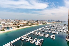 A marina with numerous boats docked, a pier extending into the water, and a coastal cityscape in the background.