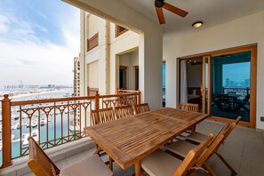 A balcony with a wooden table and chairs, overlooking a marina and cityscape.