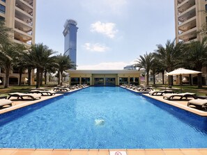 A swimming pool with lounge chairs, palm trees, and a building with balconies in the background.